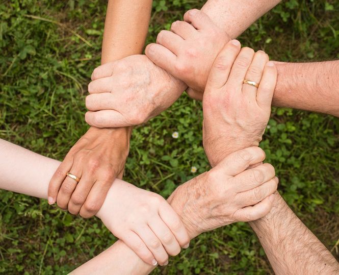 A downward shot of multiple hands grasping the wrist of the person to their right creating a circle of hands holding wrists.