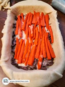 Placing a layer of carrots on top of shredded roast while making mouthwatering pot roast pie.