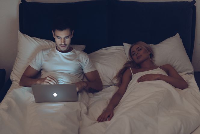 A young couple showing one of their toxic marriage habits by laying in bed and avoiding going to sleep together.