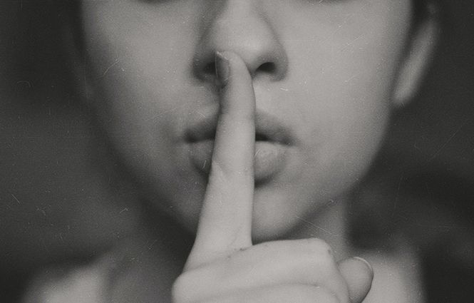 A woman with her finger over her mouth showing that she keeps secrets as one of her toxic marriage habits.
