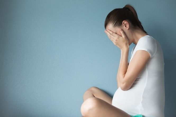 Pregnancy shaming downright sucks. This is a photo of a pregnant woman sitting on the floor and crying in her hands.