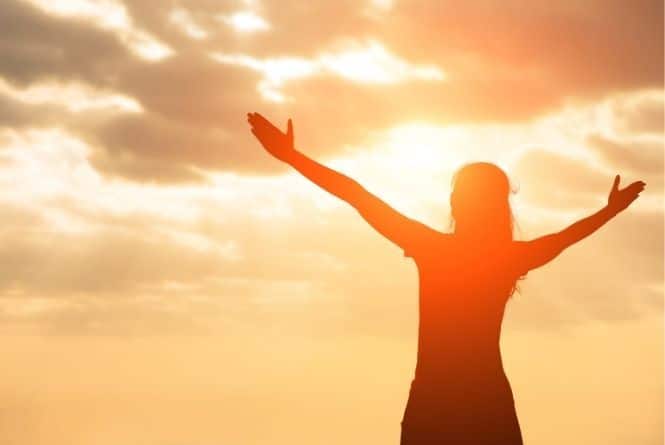 When and how to teach manners to kids includes praise. This is a picture of a woman holding her arms open and up to the sky in praise with a sunset in the background.