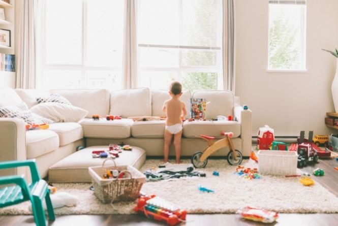 Growing your family will change your lifestyle. This is a image of a toddler in a room messy with child toys.